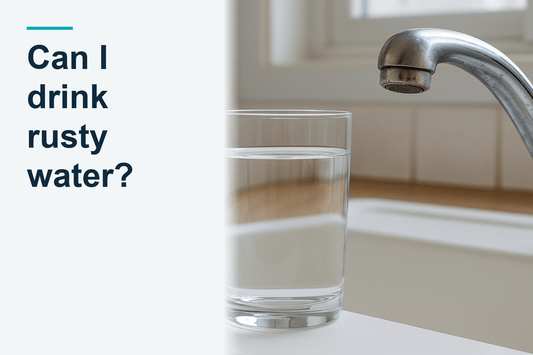 A clear glass of transparent tap water beside an aged chrome kitchen tap with subtle rust staining around the aerator, a still inspection scene with the tap