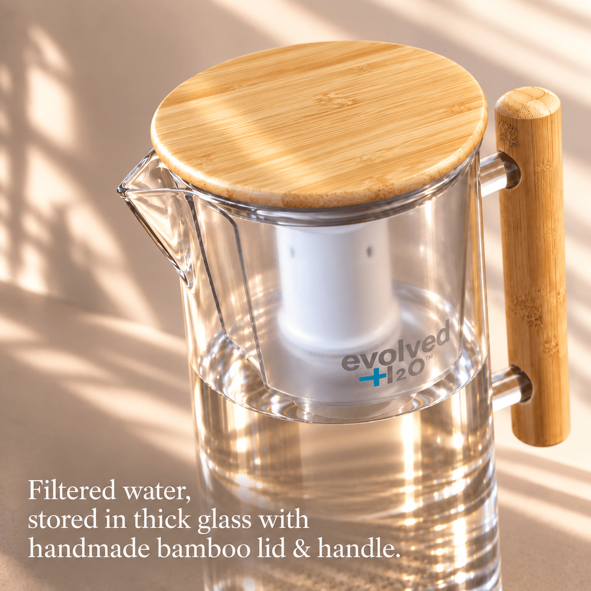 Evolved H2O glass water filter jug filled with filtered water, featuring thick glass construction and a handmade bamboo lid and handle