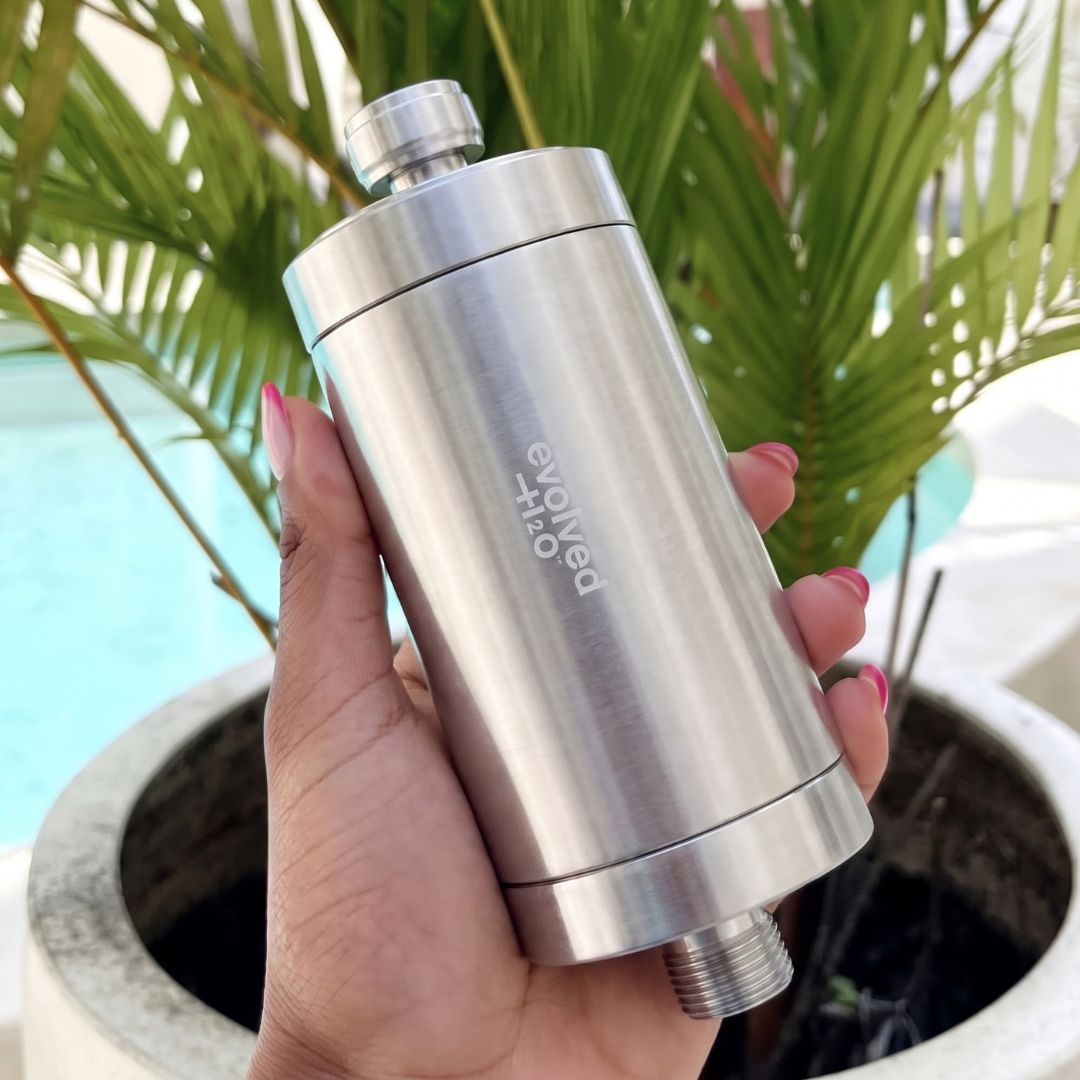 Hand holding the Evolved H2O stainless steel shower filter, showing its compact cylindrical design and threaded connections