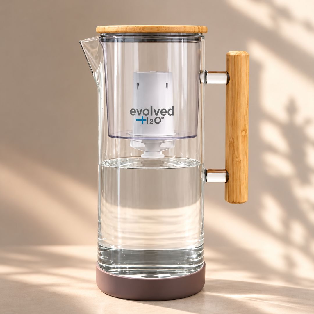 Evolved H2O glass water filter jug filled with filtered water, featuring a bamboo lid and handle with the filter cartridge visible inside