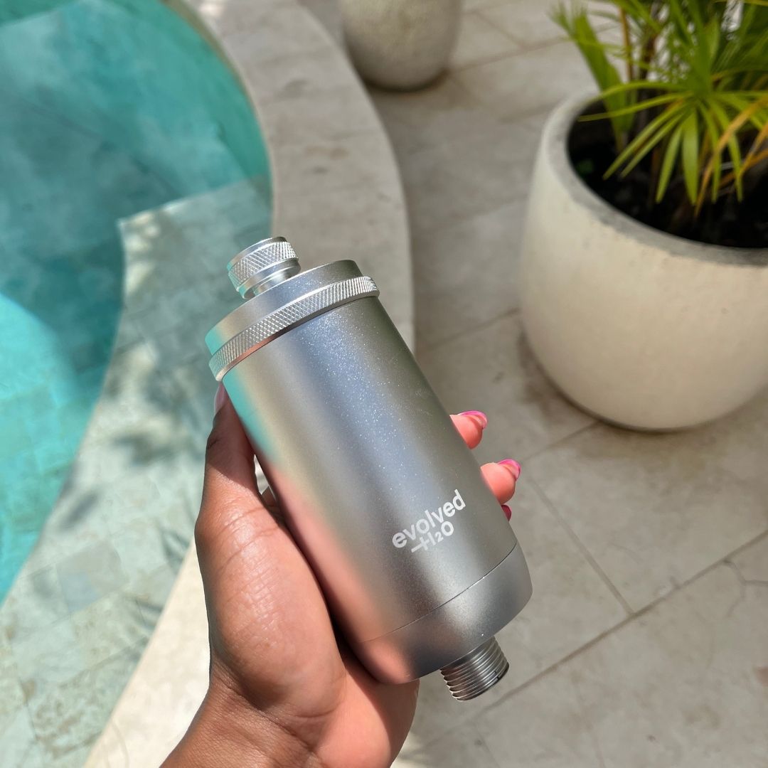 Hand holding the silver Evolved H2O shower filter beside a pool