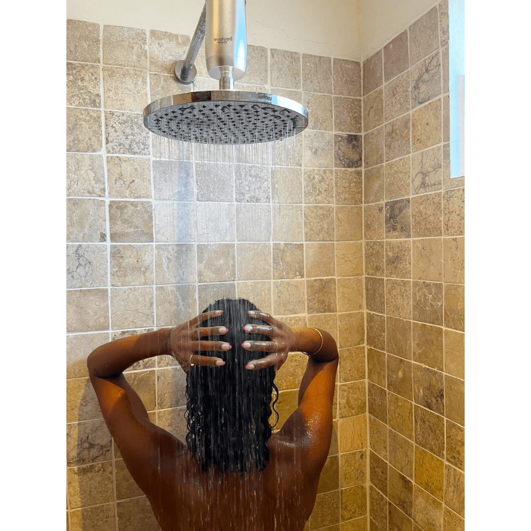 Person washing their hair beneath a rainfall shower fitted with an Evolved H2O shower filter